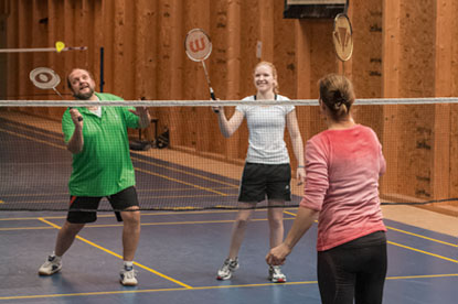 Drei Personen spielen Badminton in einer Sporthalle