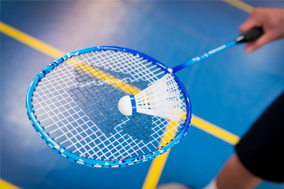 Eine Person hält einen Badminton Schläger in der Hand und balanciert darauf einen Federball.