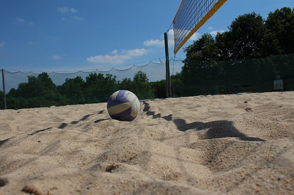 Ein  Beachvolleyball liegt auf dem Sand unter dem Netz eines Beachvolleyball Feldes.