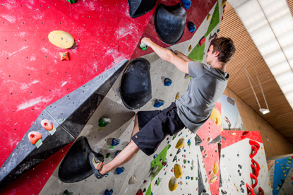Das Bild zeigt eine Person, die an einer farbenfrohen Kletterwand in einer Boulderhalle klettert.