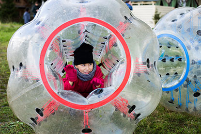 Ein Kind liegt in einer gigantischen, aufgeblasenen Bubble auf einem Fußballplatz.