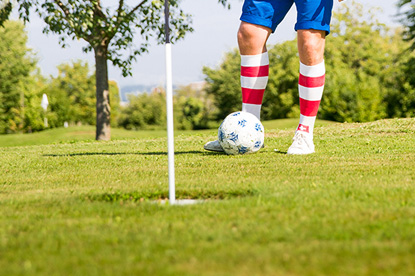 Eine Person steht mit einem Fußball vor einem Fußballgolf Loch positioniert