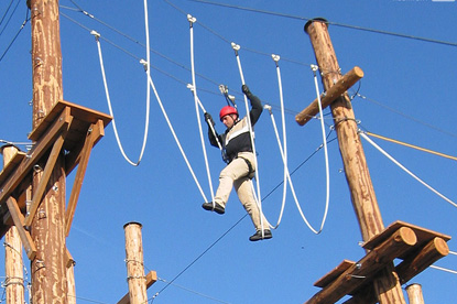 Eine gesicherte Person balanciert über gespannte Seile von Mast zu Mast in einem Hochseilgarten.