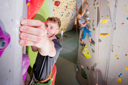 Auf dem Bild sind mehrere Personen in einer Kletterhalle zu sehen, die an Wänden mit bunten Griffen klettern