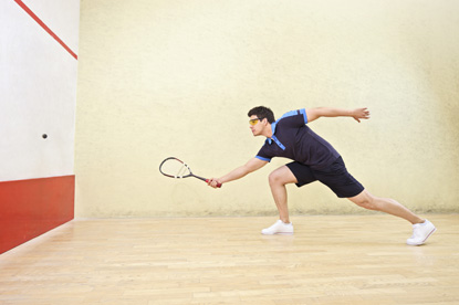 Eine Person befindet sich auf einem Squash Court und bereit sich darauf vor den Ball zu schlagen
