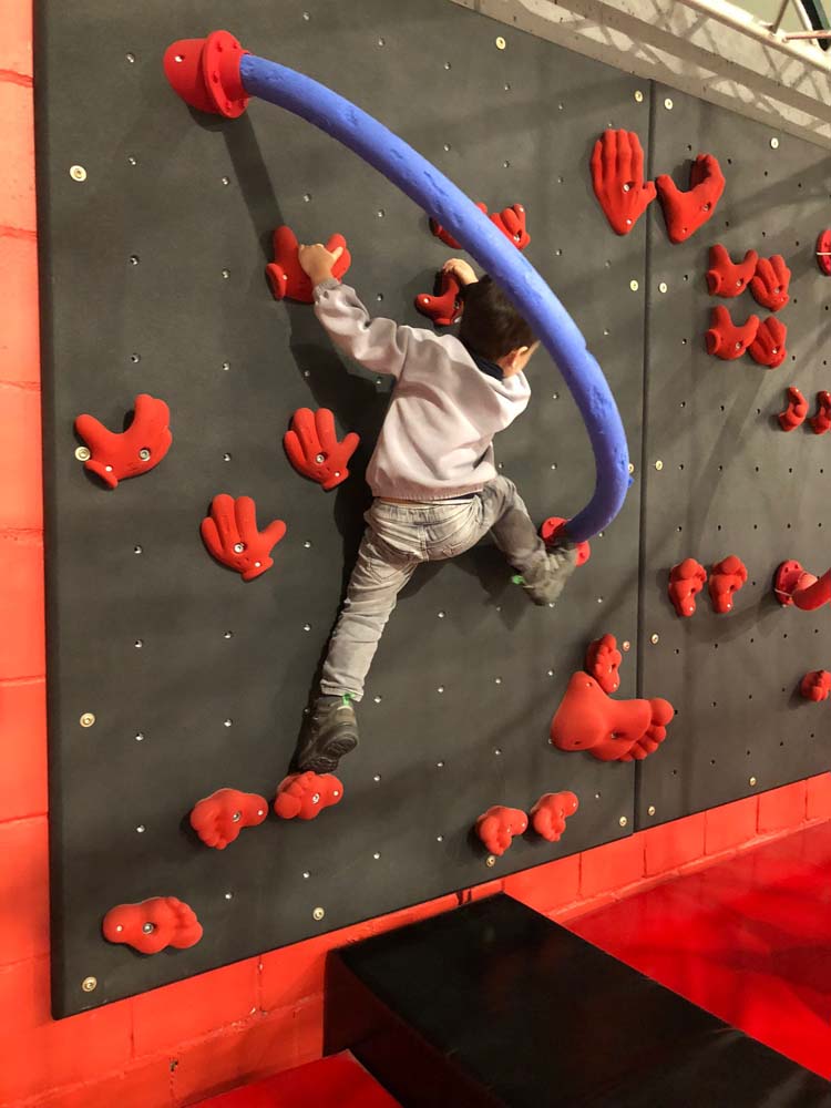 Boulderwand Ein Kleinkind klettert vertikal über eine Boulerwand.